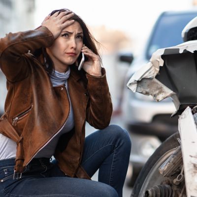 Frau hockt weinend vor beschädigtem Fahrzeug und telefoniert